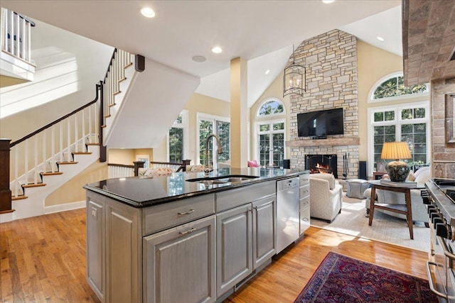 kitchen featuring sink, dishwasher, high vaulted ceiling, a kitchen island, and a stone fireplace