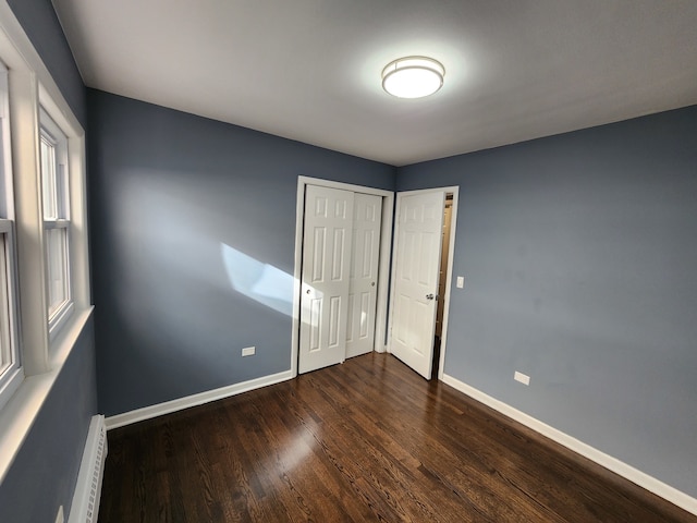 unfurnished bedroom with a baseboard heating unit, a closet, and dark hardwood / wood-style floors