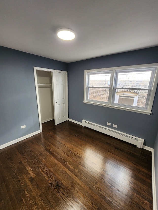 unfurnished bedroom featuring a closet, baseboard heating, and dark wood-type flooring