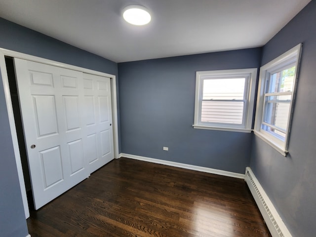 unfurnished bedroom with a closet, dark hardwood / wood-style flooring, and a baseboard heating unit