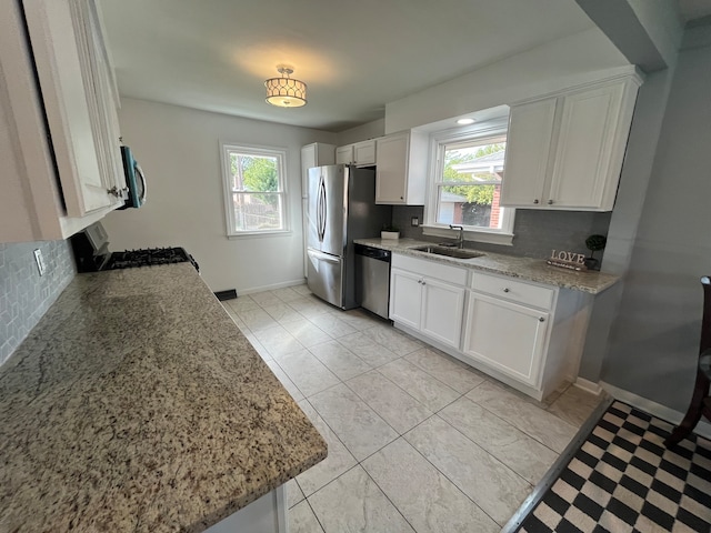 kitchen featuring stainless steel appliances, plenty of natural light, light stone countertops, and white cabinetry