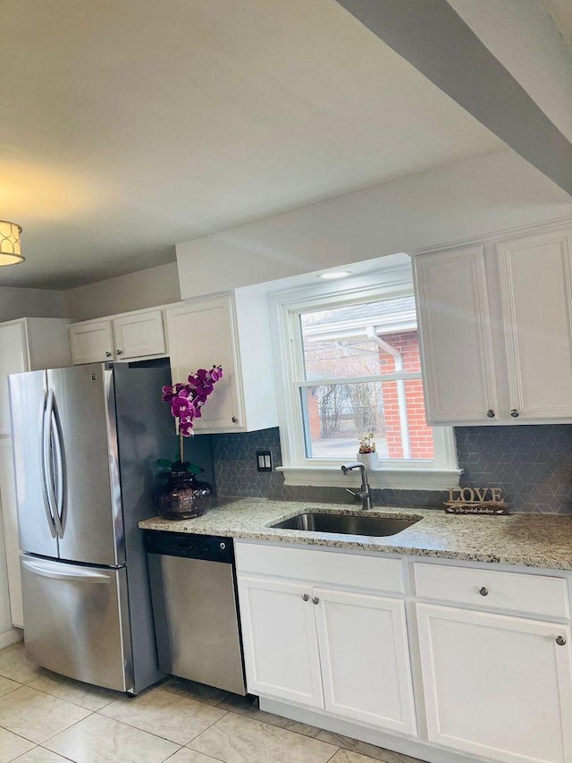 kitchen with appliances with stainless steel finishes, white cabinetry, sink, decorative backsplash, and light stone countertops