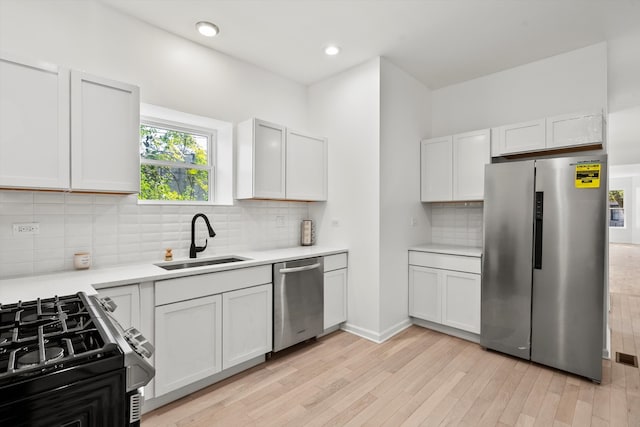 kitchen with appliances with stainless steel finishes, white cabinetry, tasteful backsplash, light wood-type flooring, and sink