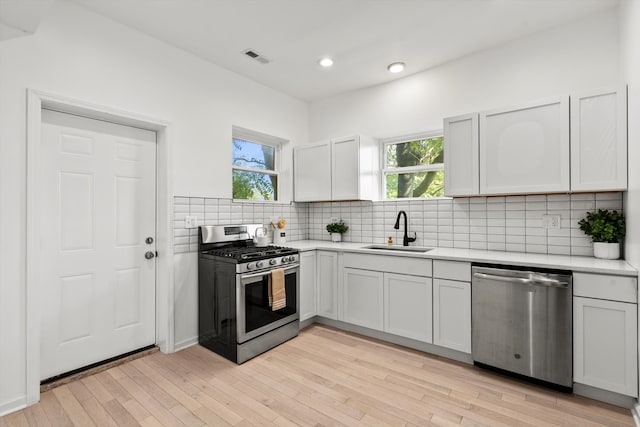 kitchen featuring white cabinetry, backsplash, stainless steel appliances, light hardwood / wood-style flooring, and sink