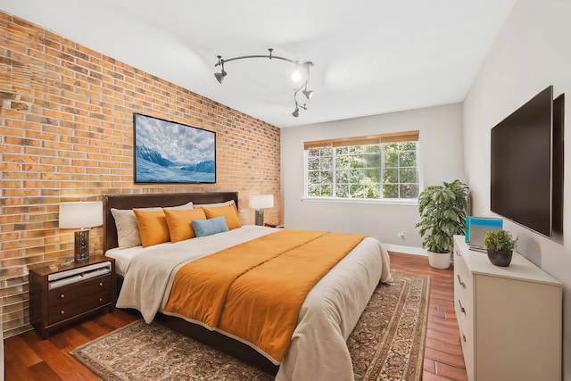 bedroom featuring brick wall, track lighting, and dark hardwood / wood-style flooring