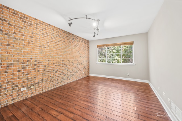 unfurnished room featuring brick wall, track lighting, and hardwood / wood-style floors