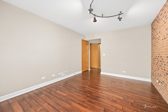 spare room featuring rail lighting, dark hardwood / wood-style flooring, and brick wall