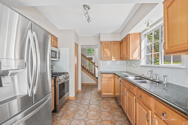 kitchen featuring appliances with stainless steel finishes, rail lighting, dark stone countertops, tasteful backsplash, and sink