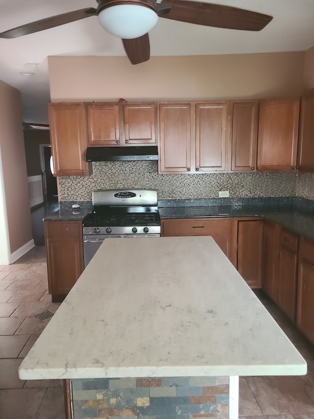 kitchen with ceiling fan, stainless steel gas range oven, tasteful backsplash, and a kitchen island