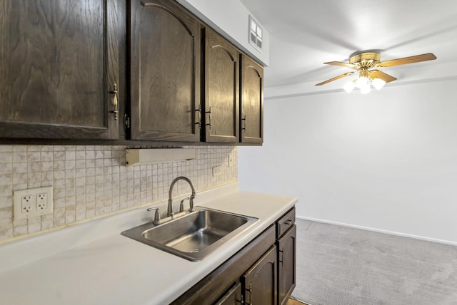 kitchen featuring dark brown cabinetry, light countertops, light carpet, decorative backsplash, and a sink