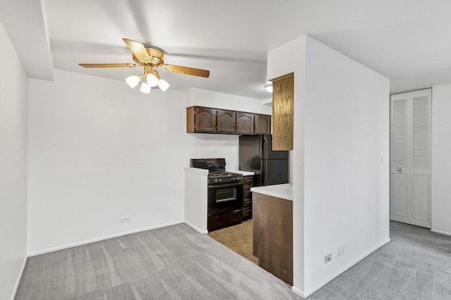 kitchen with dark brown cabinets, light colored carpet, light countertops, black appliances, and a ceiling fan