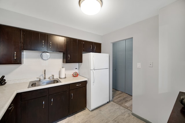 kitchen with dark brown cabinets, light wood-type flooring, white fridge, and sink