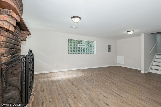 unfurnished living room featuring a brick fireplace, electric panel, and hardwood / wood-style floors