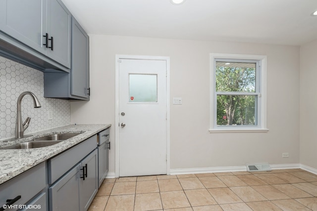 kitchen with backsplash, light stone counters, light tile patterned floors, and sink