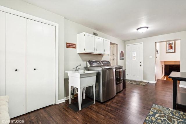 washroom featuring cabinet space, baseboards, washing machine and dryer, and dark wood-type flooring