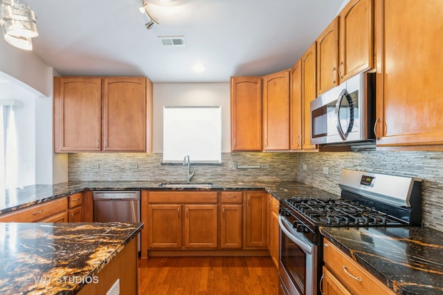 kitchen with decorative backsplash, dark stone counters, dark hardwood / wood-style flooring, sink, and stainless steel appliances