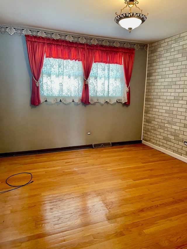 empty room featuring brick wall, hardwood / wood-style floors, and a healthy amount of sunlight