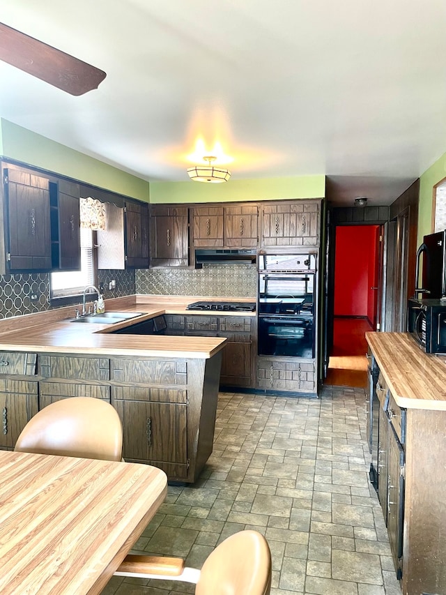 kitchen with kitchen peninsula, dark brown cabinets, backsplash, sink, and black appliances