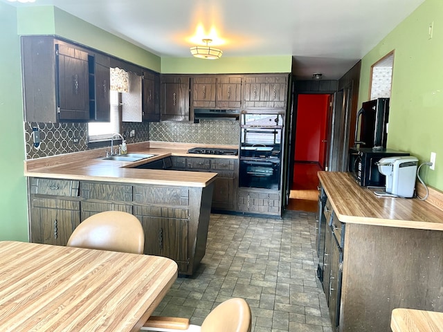 kitchen featuring sink, kitchen peninsula, dark brown cabinetry, gas stovetop, and decorative backsplash