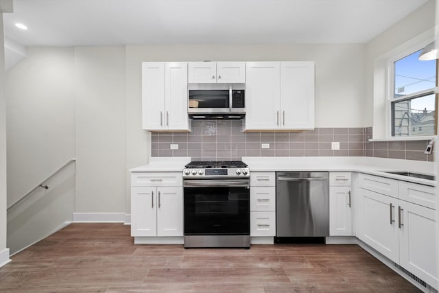 kitchen with appliances with stainless steel finishes, decorative backsplash, white cabinets, light wood-type flooring, and sink