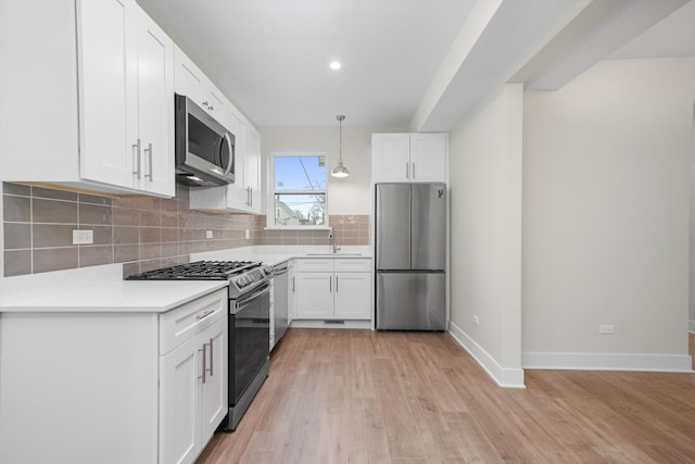 kitchen featuring appliances with stainless steel finishes, decorative backsplash, white cabinets, light wood-type flooring, and decorative light fixtures