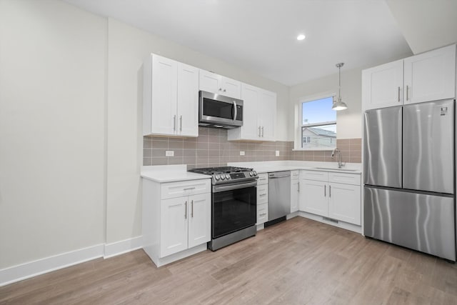 kitchen with white cabinets, appliances with stainless steel finishes, pendant lighting, and light hardwood / wood-style floors