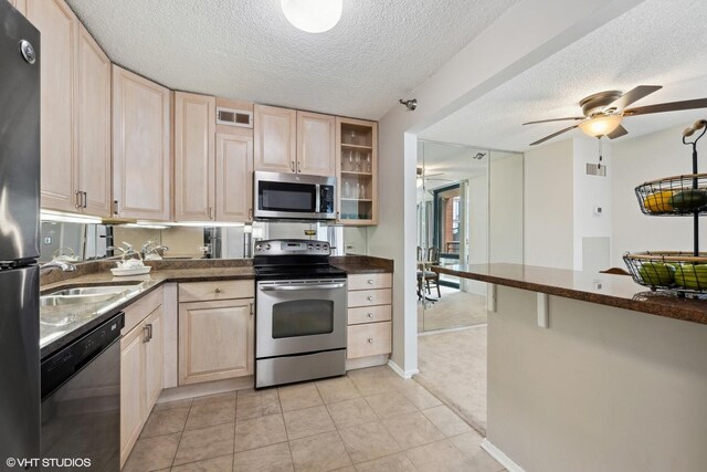 kitchen featuring appliances with stainless steel finishes, light brown cabinetry, a textured ceiling, and sink