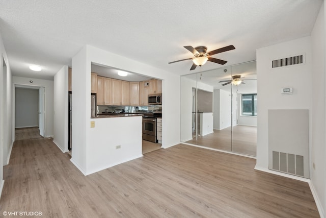 kitchen with stainless steel appliances, light hardwood / wood-style floors, light brown cabinets, and a textured ceiling