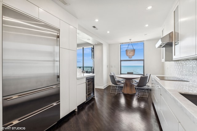 kitchen with beverage cooler, stainless steel built in refrigerator, backsplash, white cabinetry, and decorative light fixtures