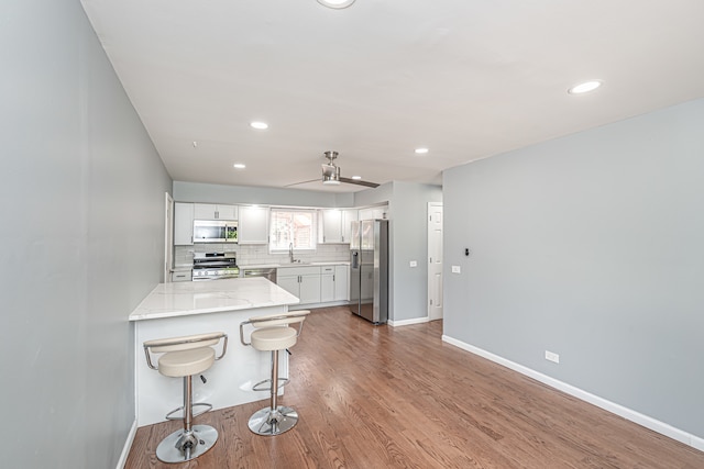 kitchen featuring hardwood / wood-style flooring, a breakfast bar area, kitchen peninsula, stainless steel appliances, and white cabinets