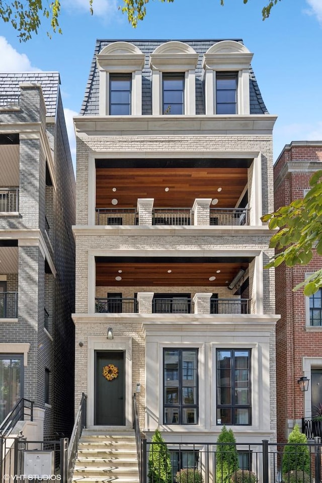 victorian home with brick siding, mansard roof, fence, and a balcony