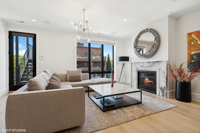 living room featuring light hardwood / wood-style flooring, a high end fireplace, a chandelier, and ornamental molding