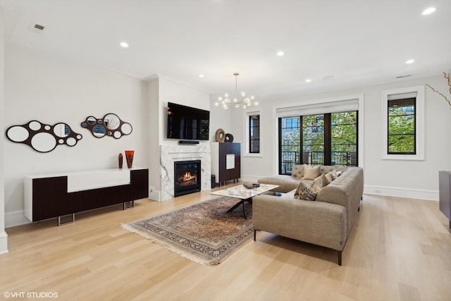 living room featuring light wood-type flooring, a premium fireplace, a notable chandelier, and crown molding