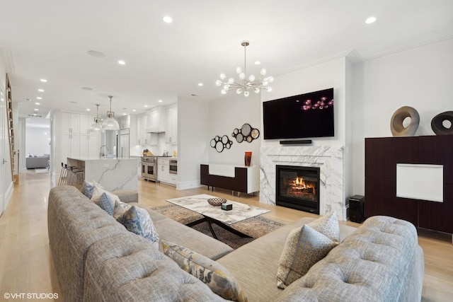 living room featuring light hardwood / wood-style flooring, a premium fireplace, crown molding, sink, and an inviting chandelier