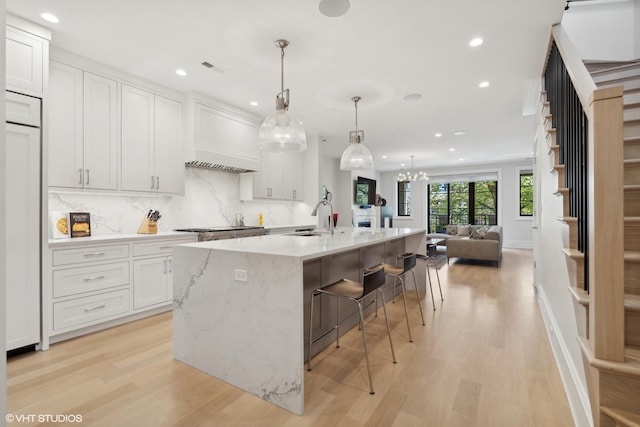 kitchen with a center island with sink, sink, white cabinetry, pendant lighting, and light hardwood / wood-style floors