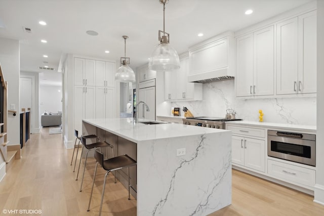 kitchen featuring decorative light fixtures, white cabinetry, a kitchen island with sink, and premium range hood