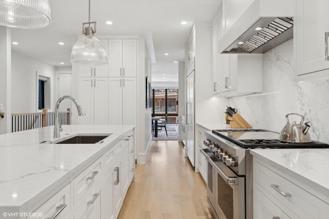 kitchen featuring decorative light fixtures, double oven range, sink, white cabinets, and wall chimney range hood