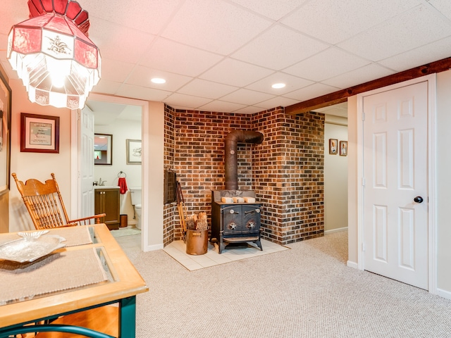 carpeted office space featuring a paneled ceiling, a wood stove, and brick wall