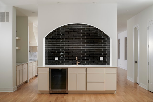 kitchen featuring sink, cream cabinets, beverage cooler, light hardwood / wood-style flooring, and decorative backsplash