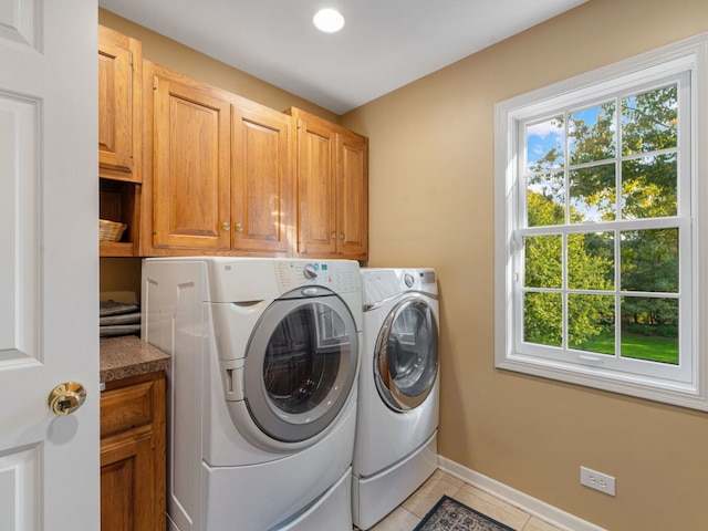 laundry area featuring cabinets, washing machine and clothes dryer, light tile patterned floors, and a wealth of natural light