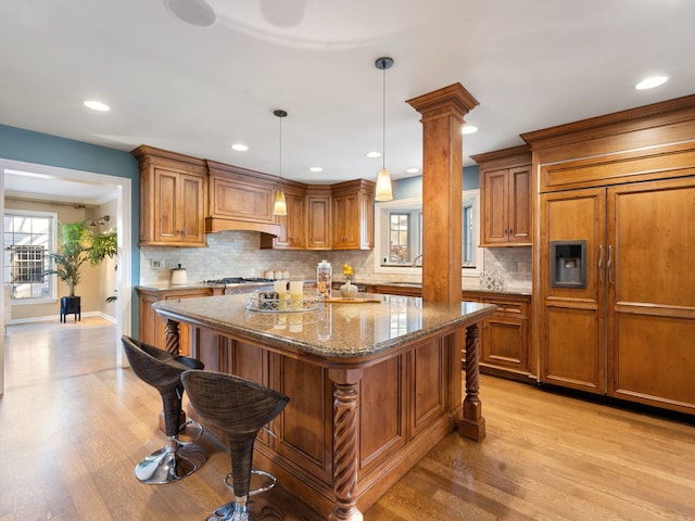 kitchen featuring light stone countertops, pendant lighting, paneled built in refrigerator, decorative columns, and a breakfast bar area