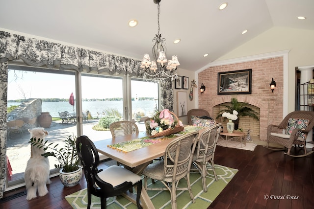 dining space featuring a water view, a fireplace, lofted ceiling, an inviting chandelier, and dark hardwood / wood-style floors