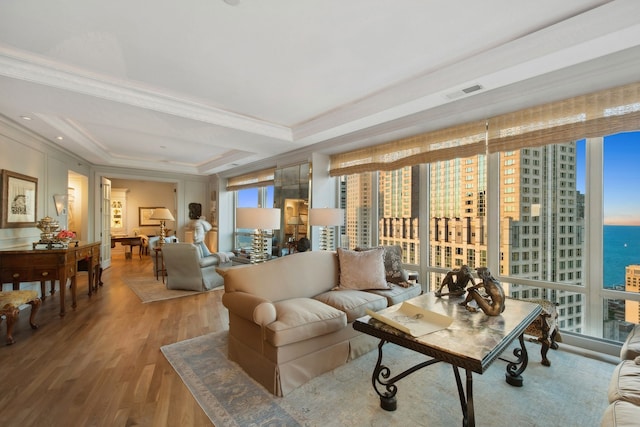 living room featuring wood-type flooring, a raised ceiling, ornamental molding, and a water view