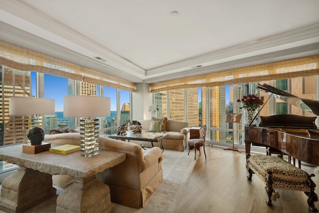 living area featuring light wood-type flooring, a raised ceiling, and crown molding