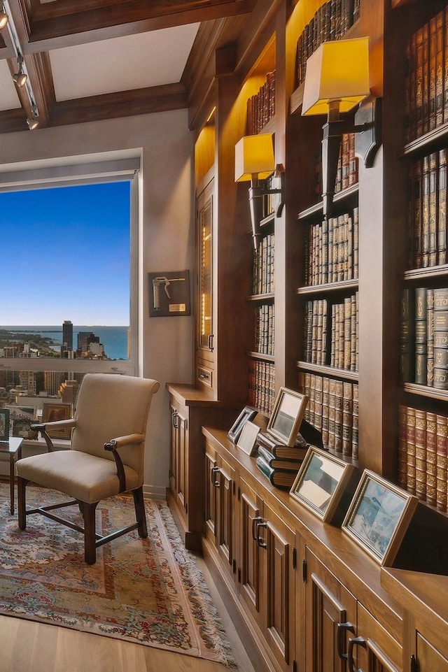 living area featuring light wood-type flooring, a water view, beamed ceiling, and coffered ceiling