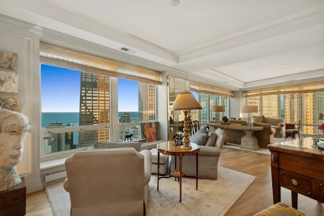 living area featuring light wood-type flooring, crown molding, a tray ceiling, and a water view