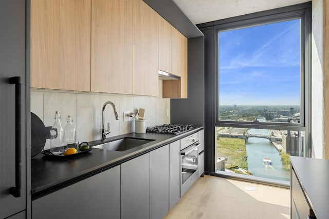 kitchen with sink, light brown cabinets, stainless steel appliances, light hardwood / wood-style floors, and decorative backsplash