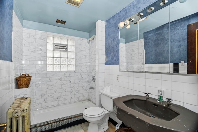 bathroom with sink, radiator heating unit, a tile shower, tile walls, and toilet