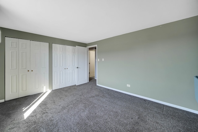 unfurnished bedroom with dark colored carpet and two closets