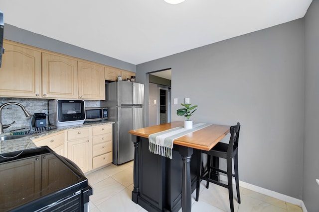 kitchen with tasteful backsplash, stainless steel appliances, light brown cabinets, sink, and a breakfast bar area